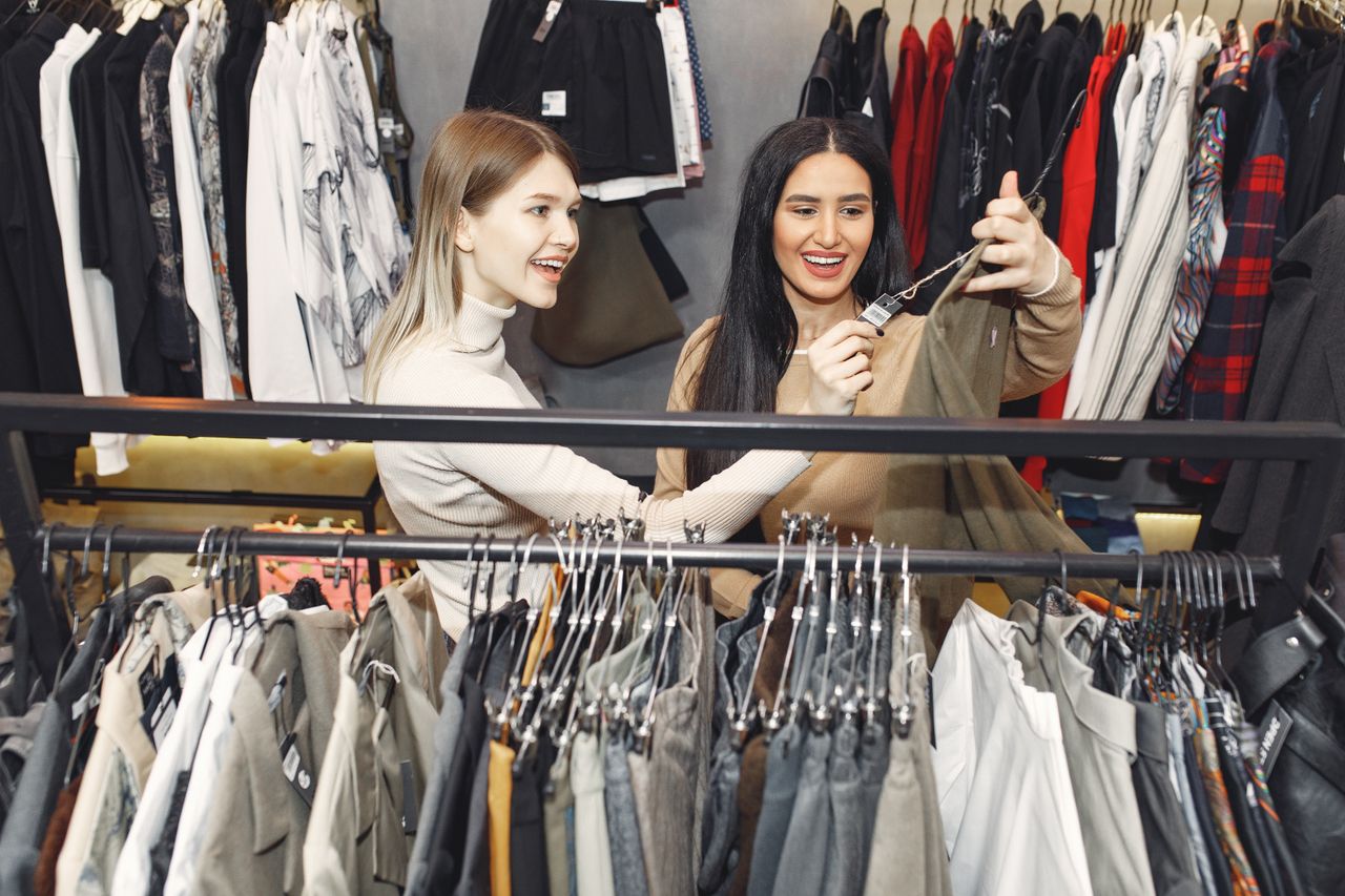 services-05 From above of young cheerful friends choosing casual pullover and laughing in shop while female looking at tag of wear