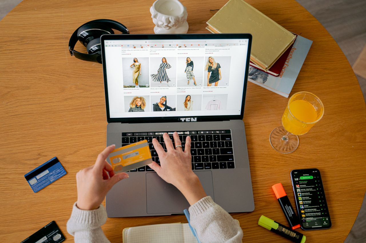 role-02 Hands holding credit card making online purchase on laptop at wooden desk with various items.