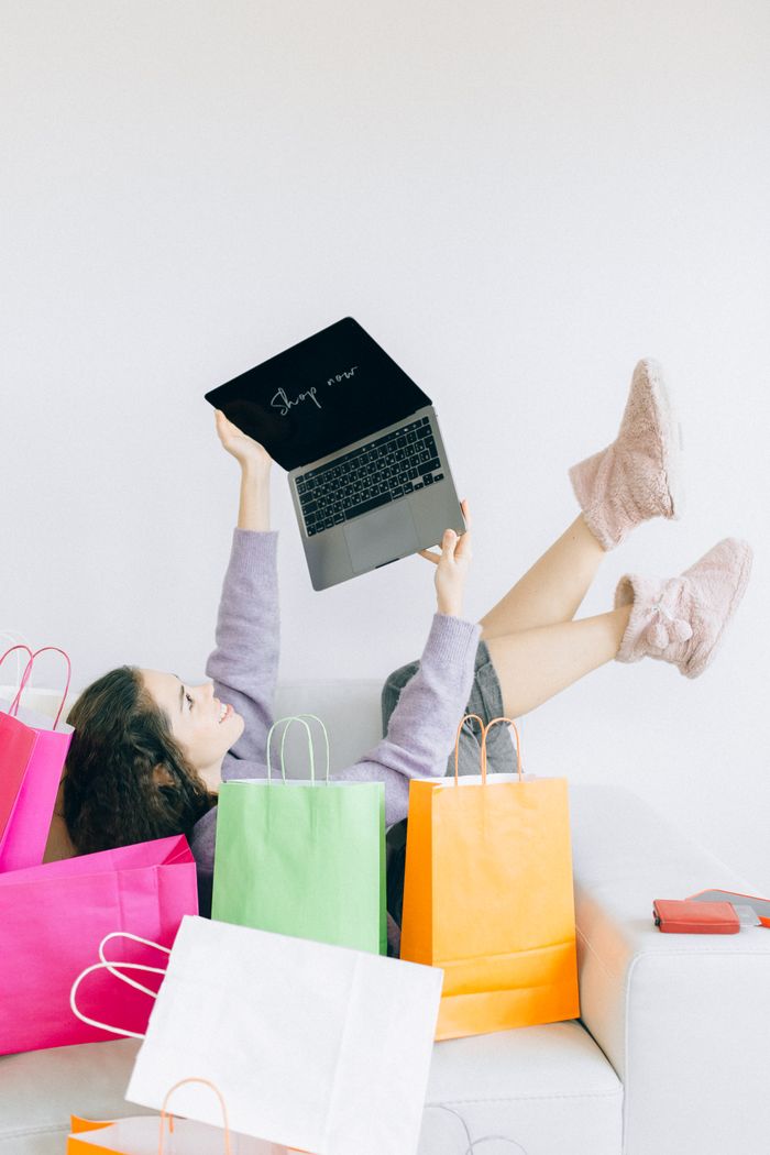 services-hero Woman lying on couch with laptop and colorful shopping bags, embodying online shopping joy.