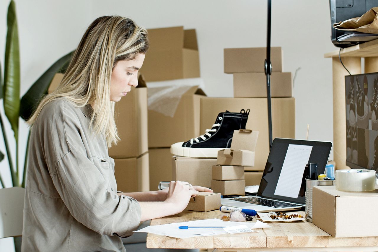 The Art of Drawing Readers In: Your attractive post title goes here A woman packing boxes for her online store, surrounded by packaging materials and a laptop.